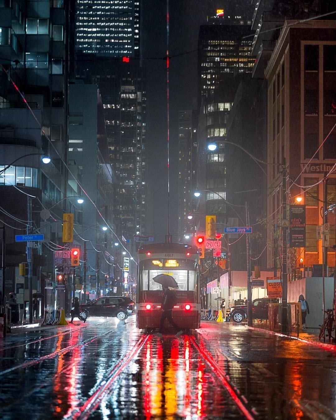 A rain-soaked Toronto street at night with the CN Tower glowing red in the distance